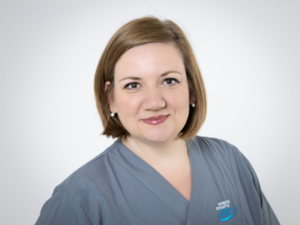 Susanne Adam mit schulterlangen Haaren, lächelt, trägt graublaue Kleidung
