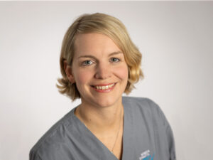 Dr. Donata Schrader mit kurzem blonden Haar, lächelt und trägt graublaue Kleidung.